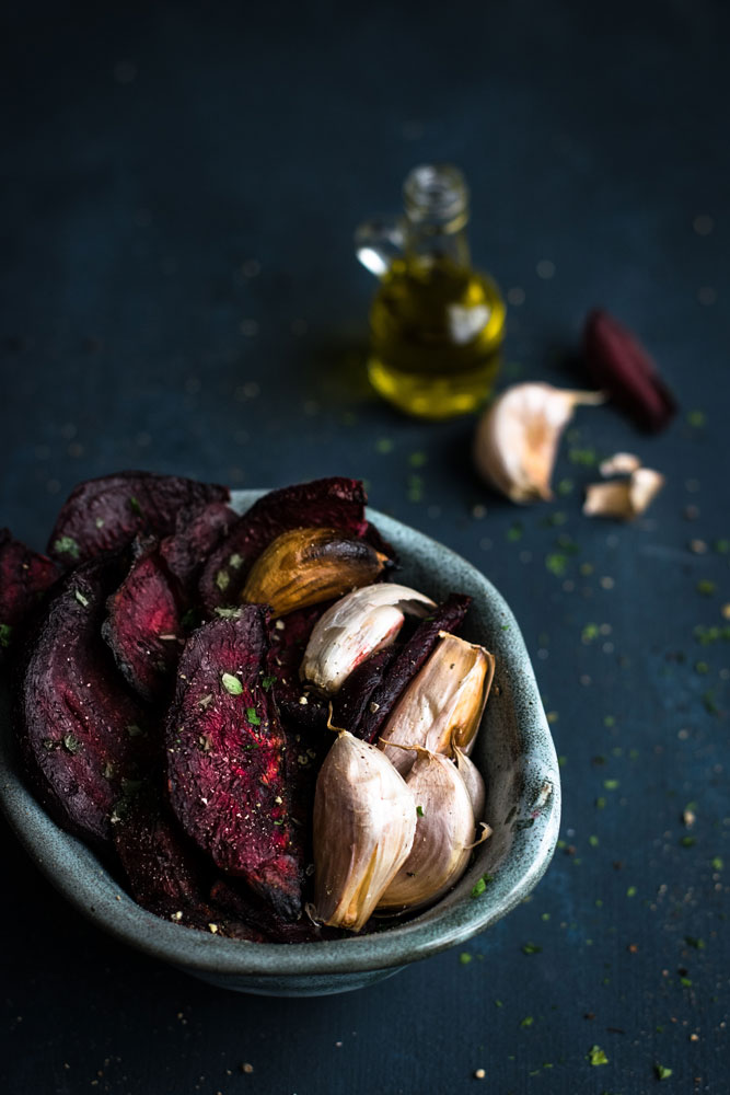 tigela com beterrabas e dentes de alho assados em primeiro plano,
com ingredientes ao fundo