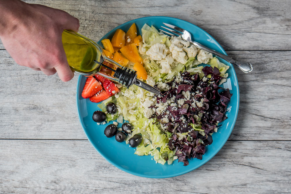 prato com mix de vegetais e mão de pessoa adicionando azeite,
vista superior